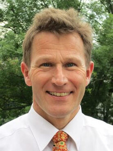 Lukas Eng mit weißem Hemd und Krawatte, draußen vor Bäumen.